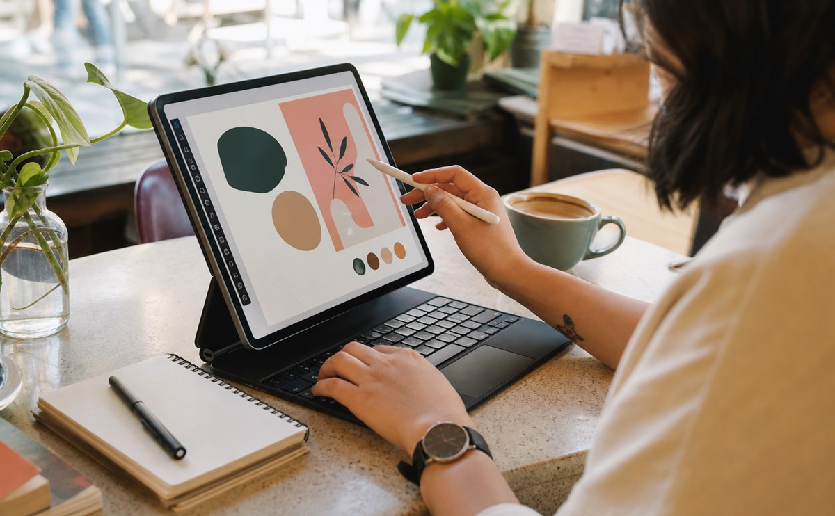 Designer working on a tablet with keyboard and stylus in a cafe